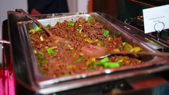 Close up of a catering tray filled with seasoned shredded beef and fresh vegetables, served in a stainless steel chafing dish during an event reception.