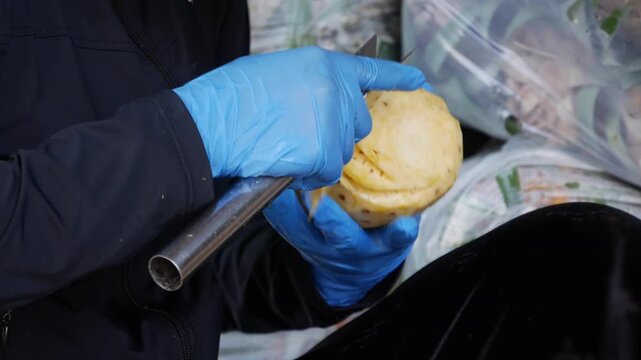 Hands in blue gloves peel and trim a pineapple with a knife at a market stall. Fruit preparation.