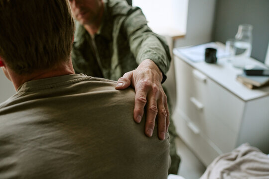 Young adult man receiving supportive shoulder touch during consultation in military hospital, representing recovery and care. Useful for veteran healthcare, trauma support, rehabilitation campaigns