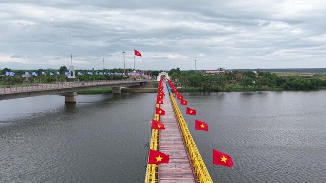 Close drone perspective looking along the Hien Luong Bridge, showing its distinctive yellow railings and rows of Vietnamese flags fluttering in the wind.