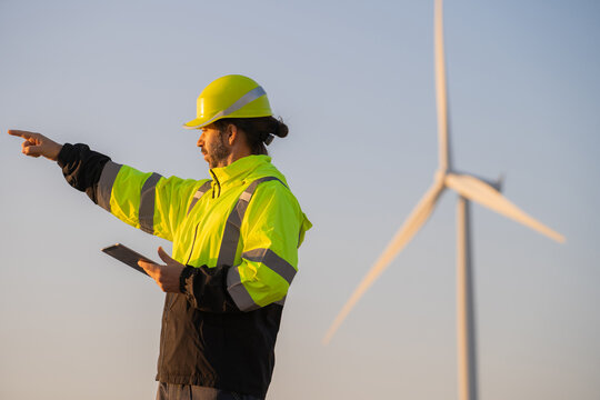 Engineer man working with tablet at windmill farm Generating electricity clean energy. Wind turbine farm generator by alternative green energy.