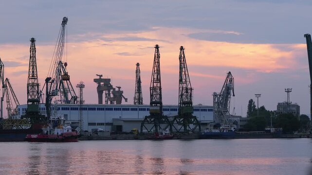 Industrial seaport cranes and tugboat at sunset