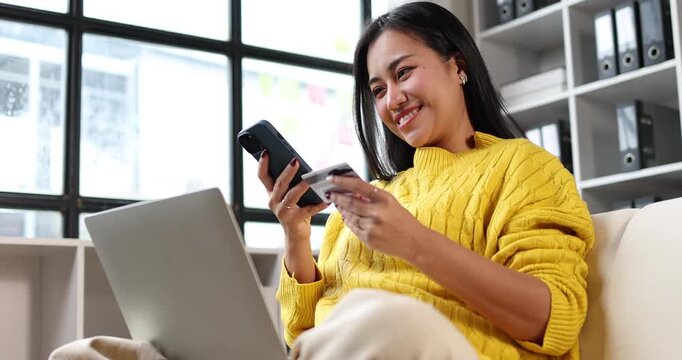 Woman sitting at home, holding a smartphone and credit card, engaged in online shopping and making secure mobile payments, utilizing digital banking for convenient purchases