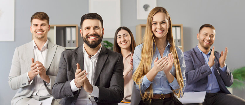 Group of smiling business professionals sitting in office and clapping hands while looking at camera. Happy corporate team expressing approval, celebrating success or showing recognition. Banner.