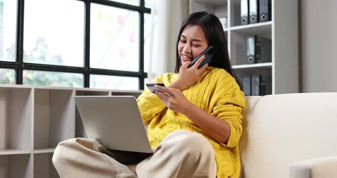 Woman sitting at home, holding a smartphone and credit card, engaged in online shopping and making secure mobile payments, utilizing digital banking for convenient purchases