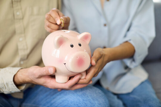 hands saving money coin in piggybank. People hold a pink piggy bank as coin drops, symbolizing savings, budget, finance and investment for future wealth. Simple view of savings growth.