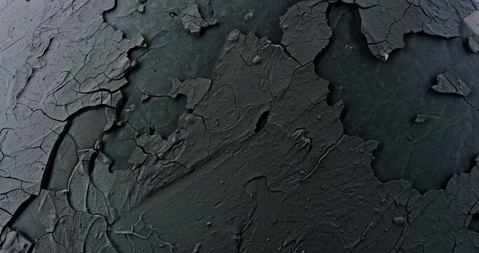 Peeling Black Paint Texture. Cracked dark coating flakes from a weathered surface during a slow rotation. For grunge and decay backgrounds.