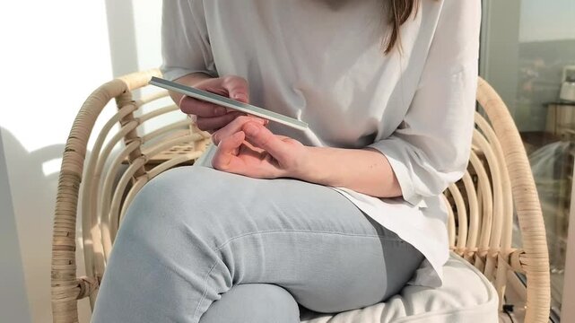 Buffer smooths nail surface and rough skin during manicure at home. Female performs selfcare routine treating fingernails carefully. Beauty concept highlights hygiene and grooming indoors..