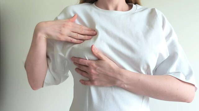 Woman lifts her shirt and feels her breast checking for lumps with her hand. She performs a self examination searching for unusual changes in her chest. Concept of breast self exam, cancer