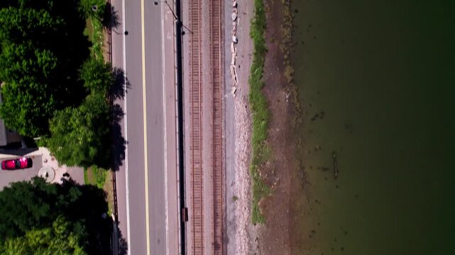 A drone flies looking traight down from a height at a road, train tracks, and a river coast in Salem, Massachusetts.