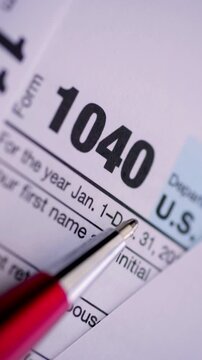 US Income Tax Form 1040. Macro view of a red pen pointing at federal tax documents with shallow depth of field.