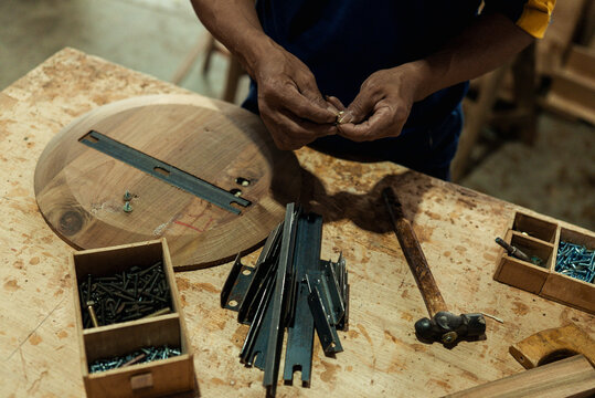 Craftsman sorting metal screws and hardware parts on a messy wooden workbench.