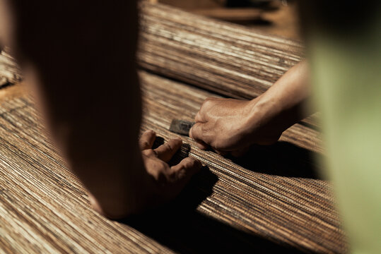 Selective focus of craftsman hand cutting a rustic woven mat with a sharp tool.