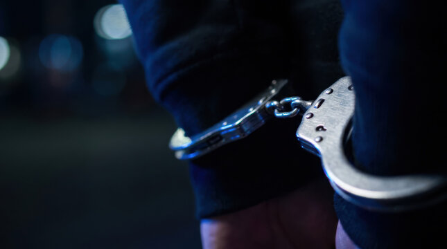 Handcuffs on wrists of person in dark clothing, symbolizing arrest and law enforcement at night