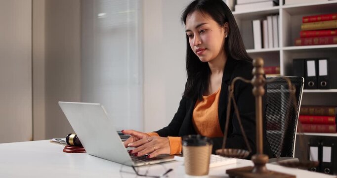Female lawyer working on laptop, researching cases and legal documents in a law office or firm, representing justice and legal assistance concepts