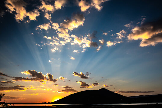 Sunlight beams from behind a silhouetted hill at sunset
