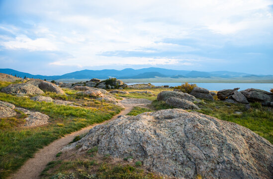 A dirt trail winds through rocks to a mountain lake