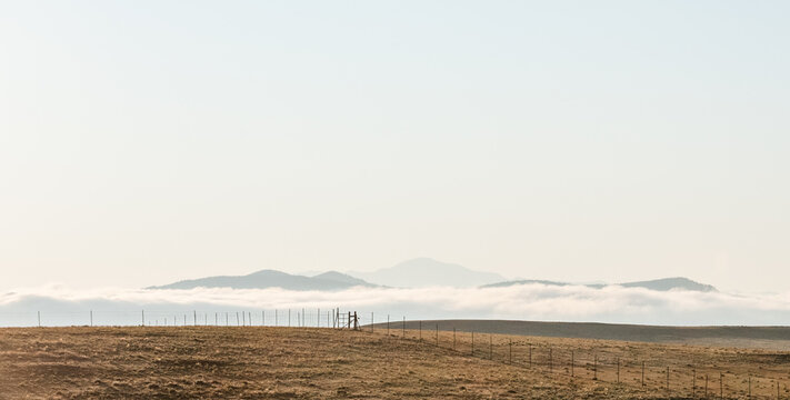 Grassy hill with fence overlooking misty mountains