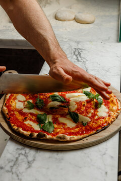A pizzaiolo cuts a freshly made pizza with a knife. Isolated