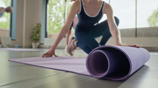 Young Caucasian woman unrolling purple yoga mat on floor in fitness studio. Clip is perfect for promoting wellness apps, healthy lifestyle brands, and gym classes