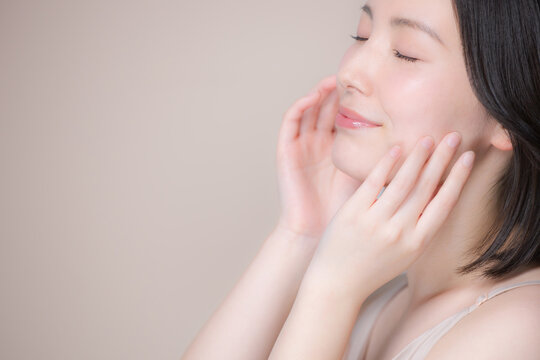ピンクベージュ背景笑顔の美しい目を閉じる日本人女性の手を触れる横顔　美しい肌とナチュラルメイクの美容クローズアップポートレート