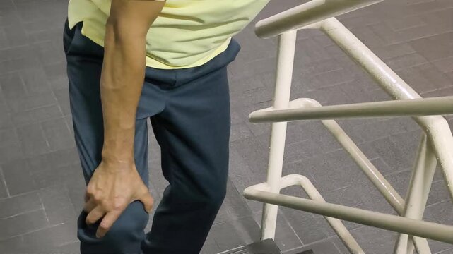Old Asian senior man hand holding knee joint pain while walking up the stair, concept of osteoporosis, thin bone, osteoarthritis; gout, knee bone joint injury problem issue, hand closeup