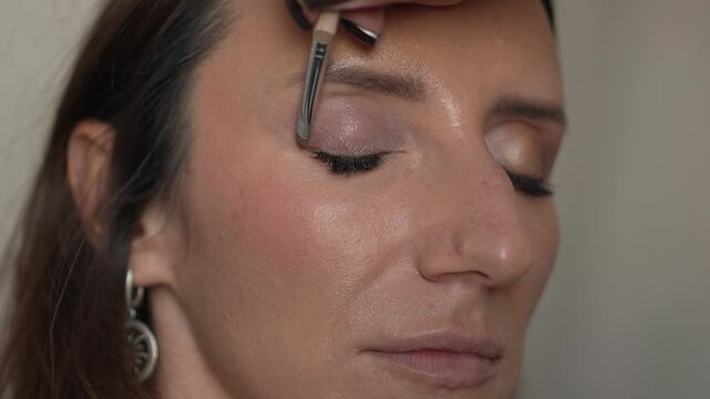 Makeup, woman, beauty expert applies natural eyeshadow to female model's closed eyelid
