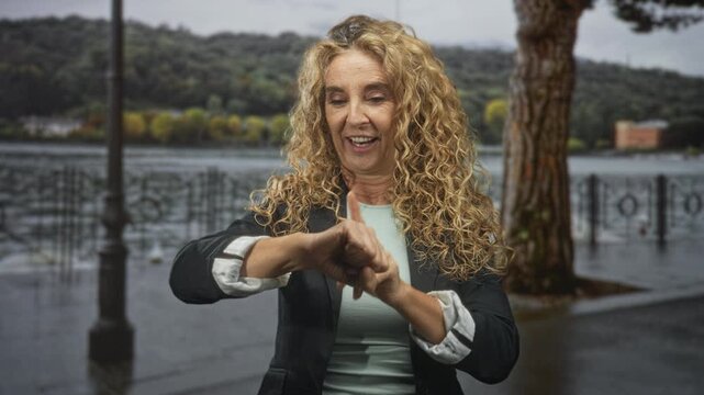 Woman checks wrist and adjusts cuff on lakeside street promenade, smiling and looking at her hands; waiting punctuality calm.