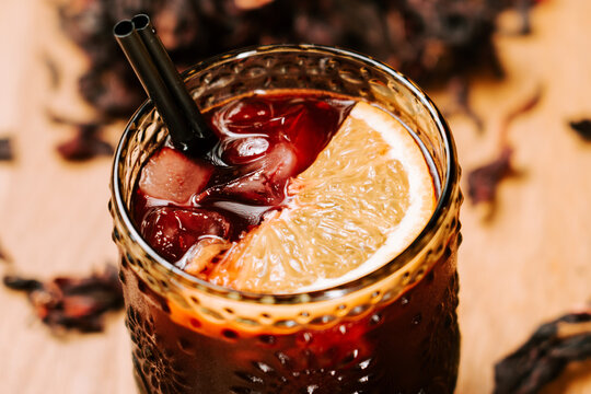 Refreshing glass of iced hibiscus tea served with a fresh orange slice during a warm sunny afternoon