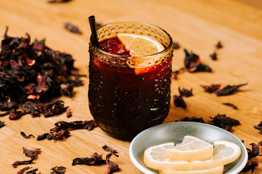 Refreshing hibiscus tea served in a patterned glass with fresh lemon slices on a wooden table
