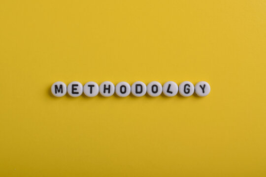 Methodology spelled with letter beads on a bright yellow background, representing structured processes, research methods, planning, organization, workflow, and business strategy.