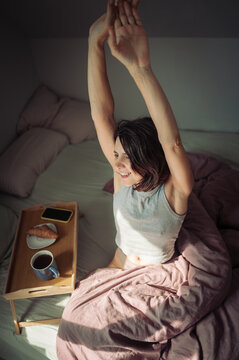 Smiling adult stretching in bed with breakfast tray