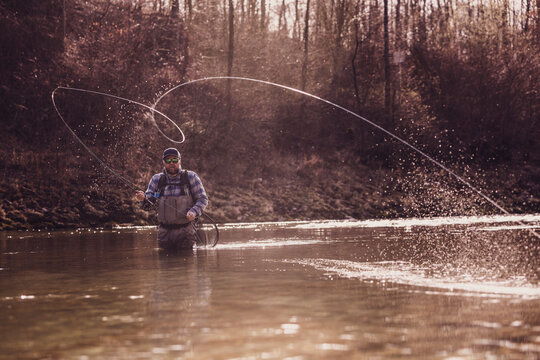 Mid adult man throwing fishing reel in river to catch fish during sunset
