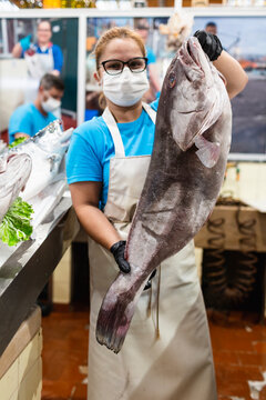 Fishmonger holding a large grouper at an indoor fish market