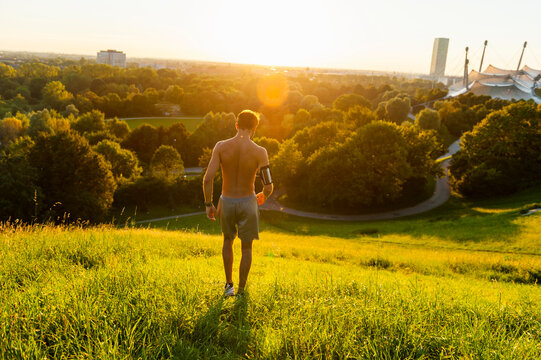 Barechested athlete on meadow in park at sunset
