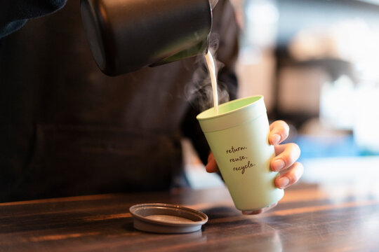 Man pouring hot milk into deposit cup for Coffee to go, close-up