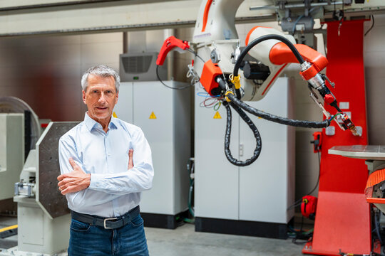 Male engineer stands indoors by an industrial robot