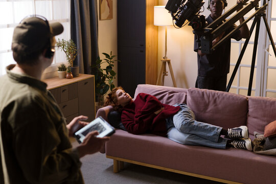 Film crew working on set with actress lying on sofa