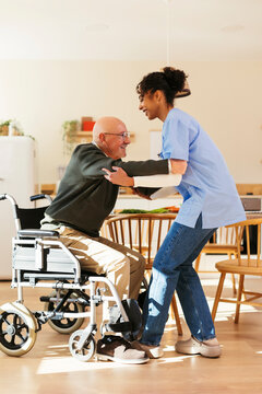 Home caregiver helping senior man in getting up from wheelchair