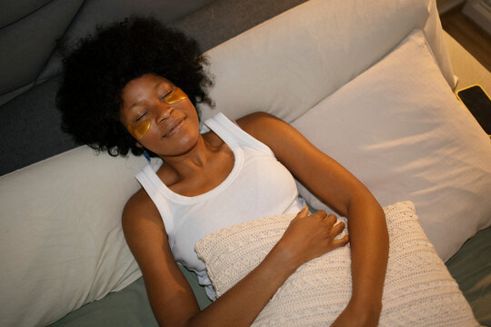 Woman relaxing in bed with eye patches practicing face care ritual
