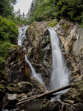 A long exposure shot of Lolaia Waterfall in Retezat National Park, Romania, showing a silky smooth water flow cascading over mossy rocks in a dense, lush green forest.