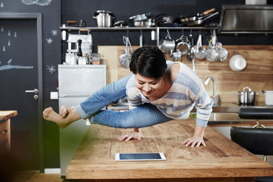 Woman doing a handstand on table in kitchen looking on tablet