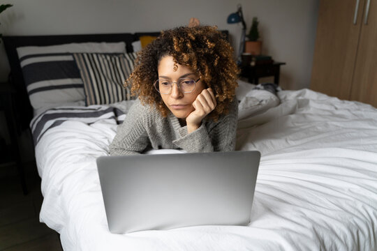 Woman lying on bed, using laptop, surfing the net