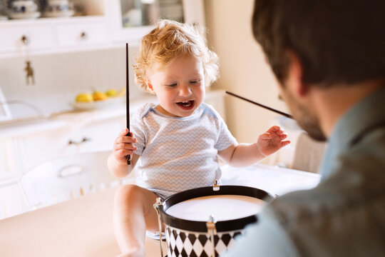 Father with happy little boy sitting on kitchen table playing drum