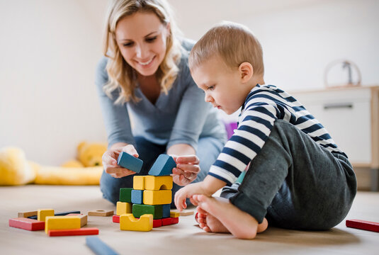 Smiling mother and toddler son playing with building blocks at home