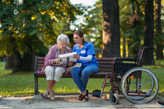 Healthcare worker with senior woman reading newspaper in park