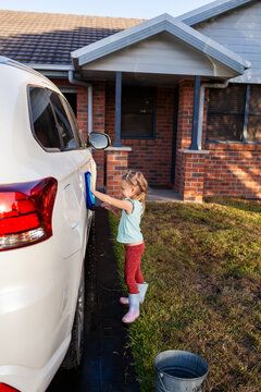 Young child helping wash family car parked on driveway in suburban front yard