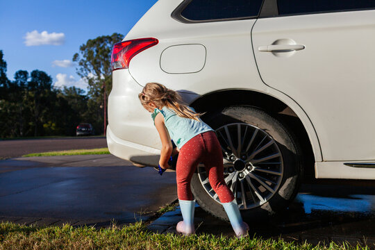 Young child helping wash family car parked on driveway in suburban front yard