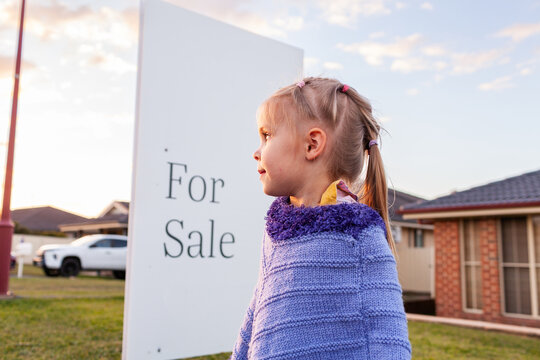 child by for sale sign outside house in suburb at dusk