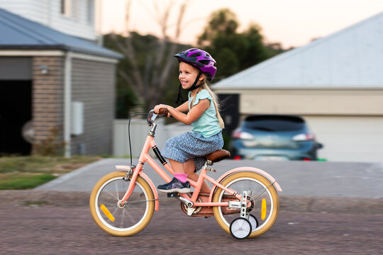 Panning movement shot of preschooler riding pink bike with training wheels on roadside